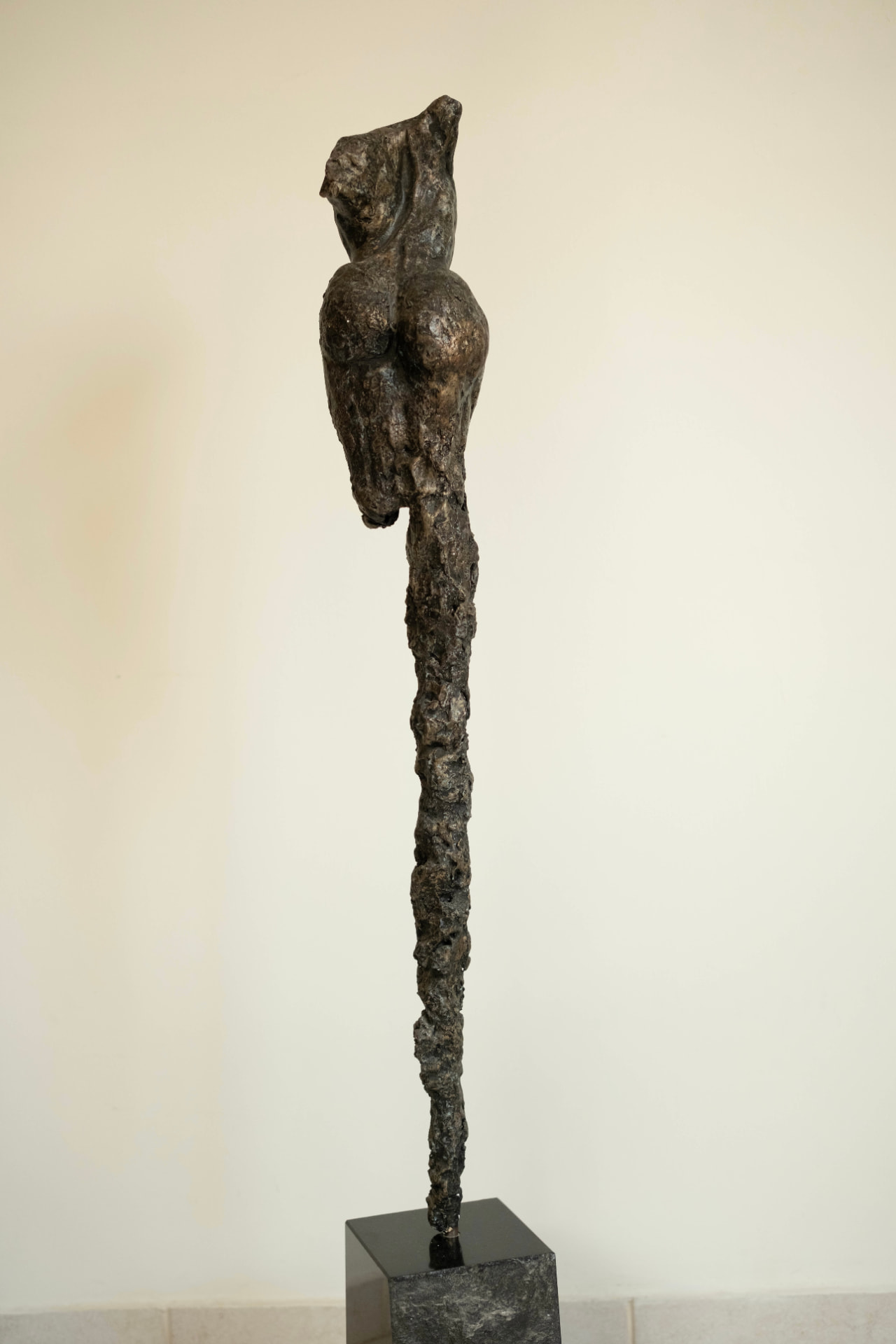 Sentinel — elongated bronze figure on a dark stone base